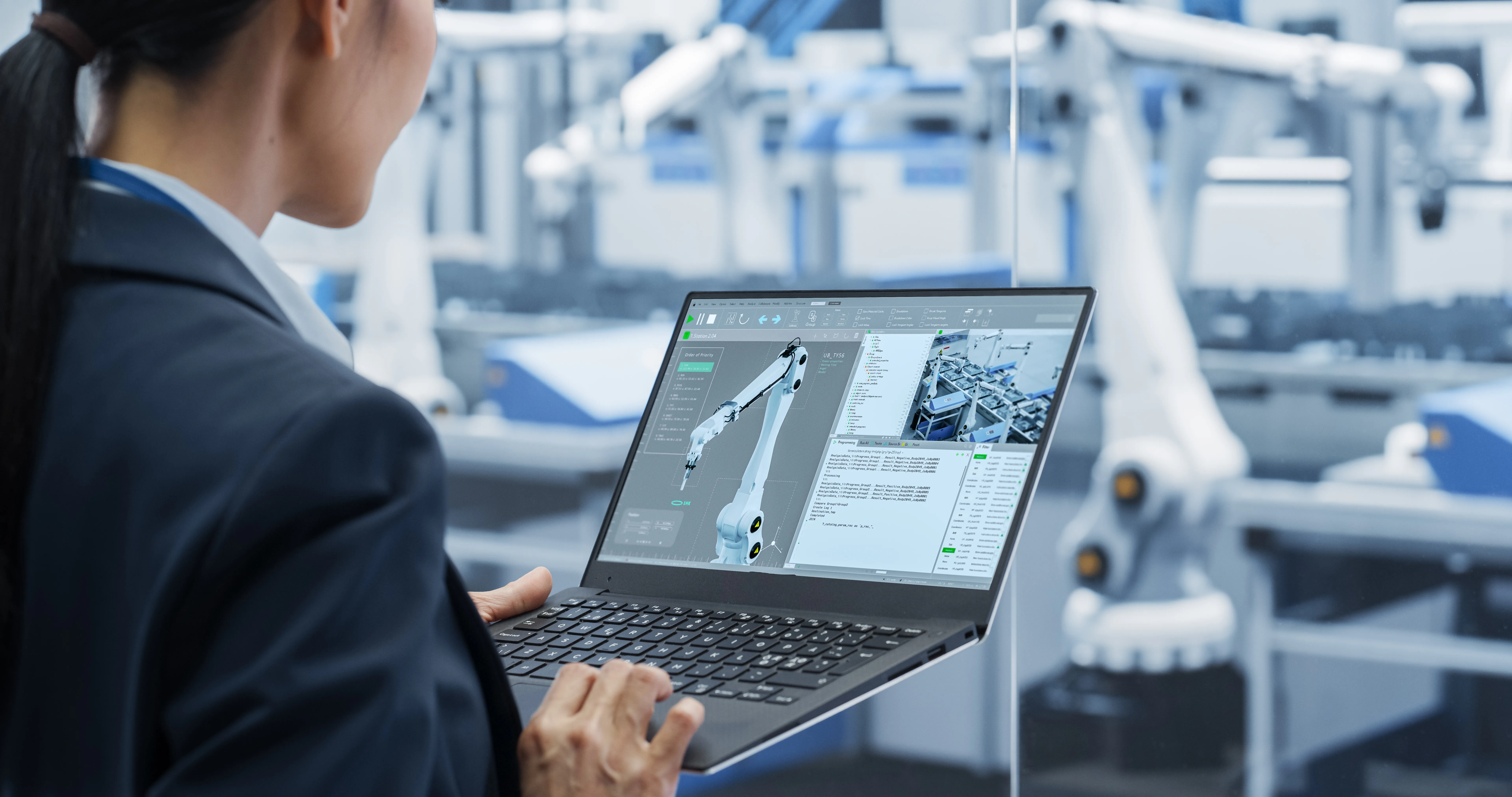 Engineer monitoring a robotic assembly line on a laptop in a factory